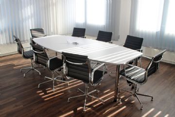 Immagine riportante un ufficio con un tavolo da lavoro attorniato da 8 sedie vuote